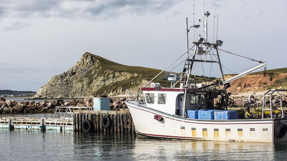 A fishing boat docked at a pier with a rocky hill in the background.
