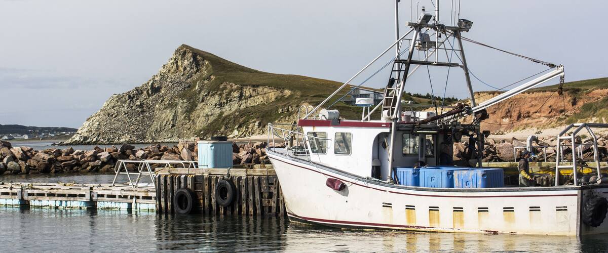 A fishing boat docked at a pier with a rocky hill in the background.