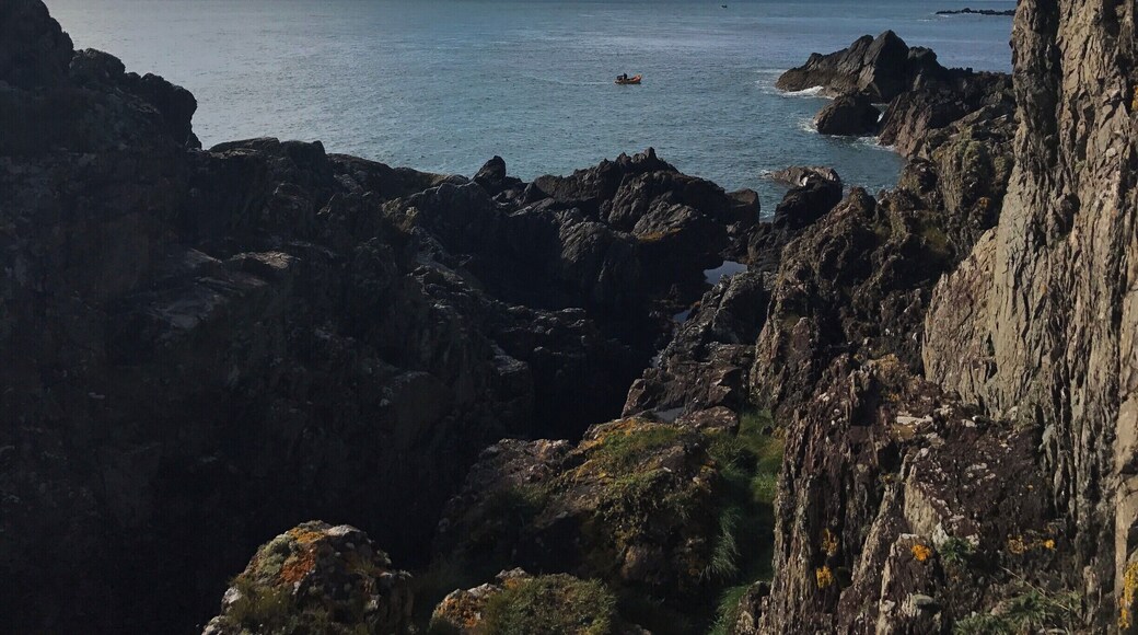 A lonely fisherman in his boat sheltered by the crags.