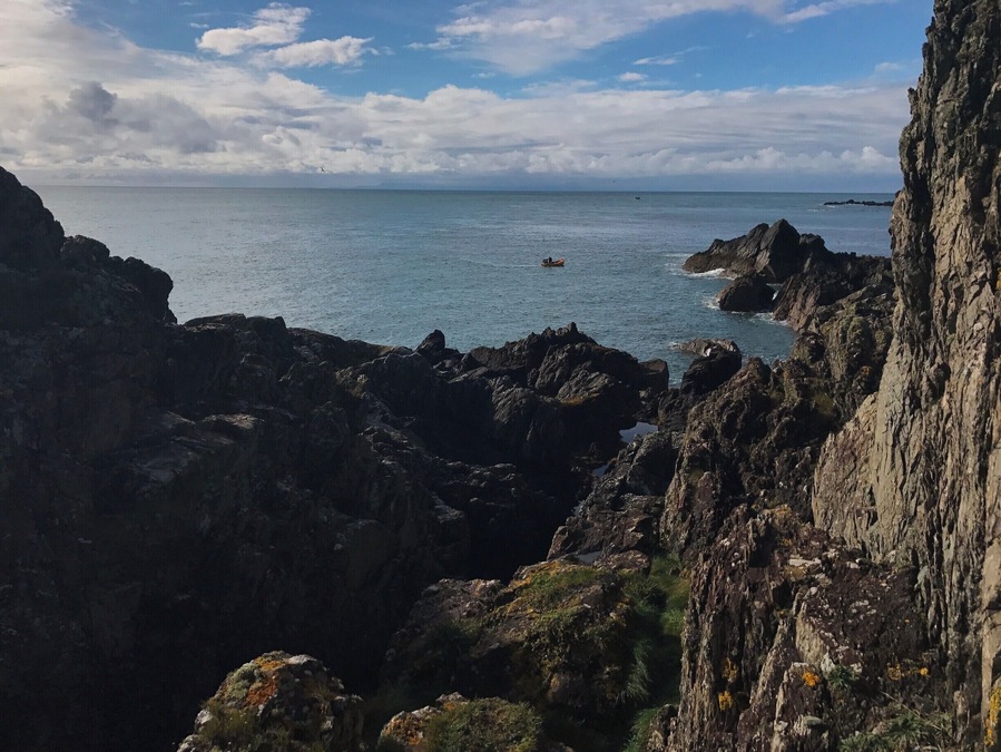 A lonely fisherman in his boat sheltered by the crags.