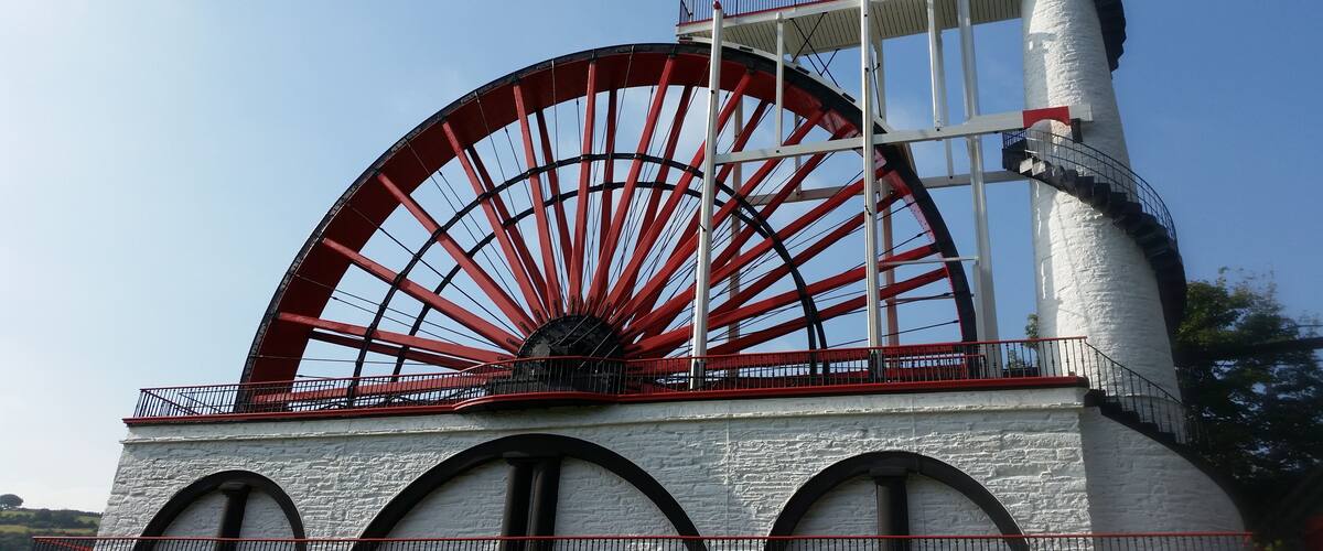 A large water wheel with red spokes, a white tower, and a red flag on top.