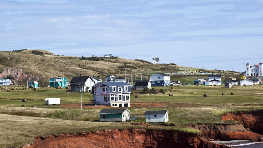 Eine Küstenlandschaft mit Häusern, einem Strand und einer Klippe mit roten Felsformationen.