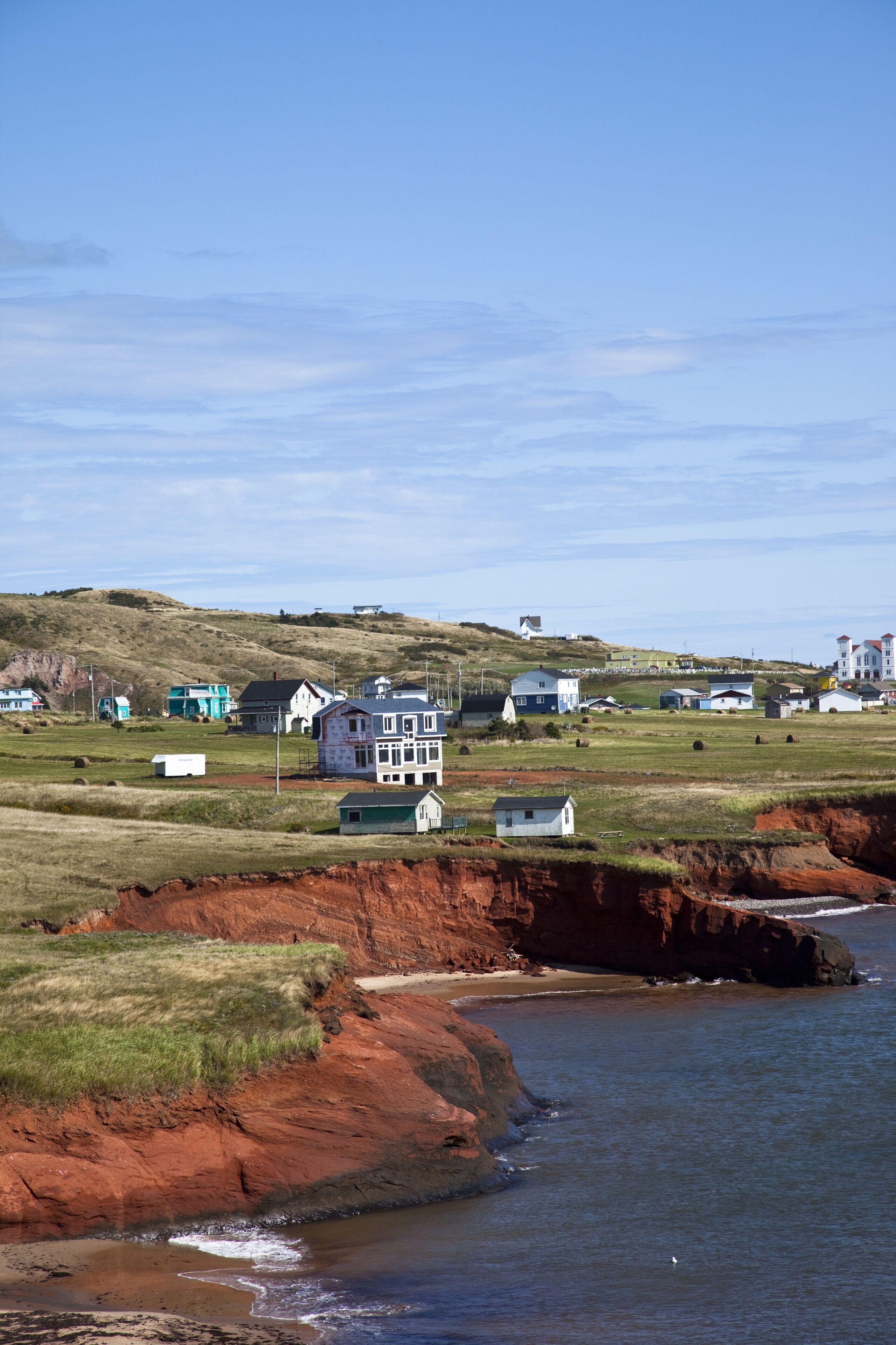 A coastal landscape with houses, a beach, and a cliff with red rock formations.