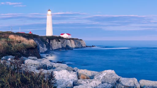 Un paisaje costero con un faro blanco destacado, acantilados rocosos y un edificio de techo rojo.