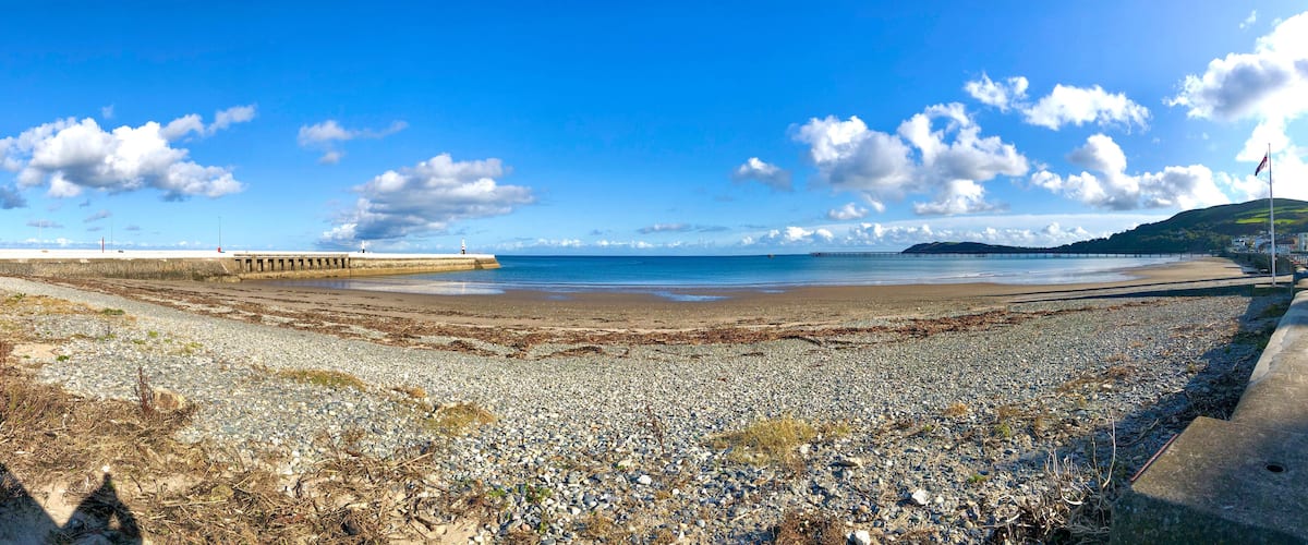 A pebbly beach with a pier and a lighthouse in the distance.