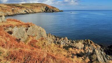 A coastal landscape with rocky cliffs, a small white building, and calm sea.