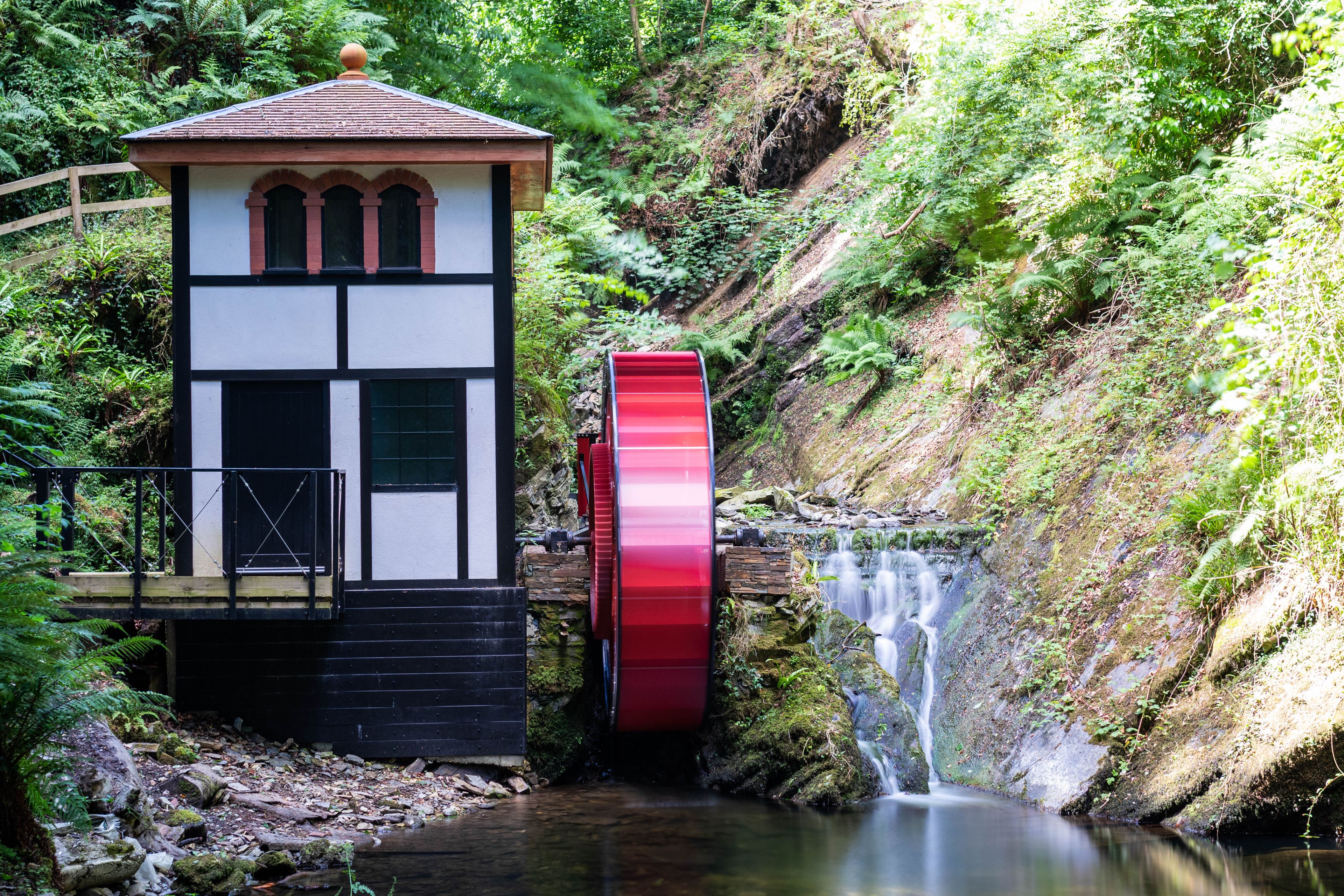 Ein rotes Wasserrad, ein kleines Gebäude mit Ziegeldach und ein Wasserfall.