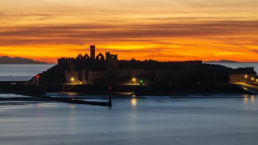 Majestic silhouette of Peel Castle ruins at dramatic sunset, Isle of Man. Long exposure shot of historic Viking fortress on St Patrick's Isle during golden twilight with smooth sea.