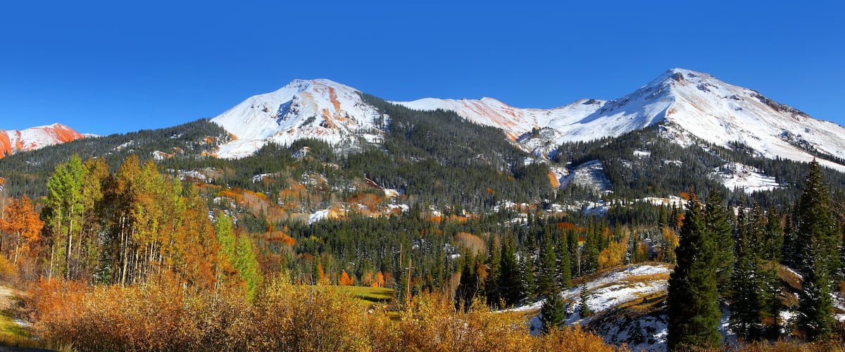 A mountain range with snow-covered peaks and autumn-colored trees.