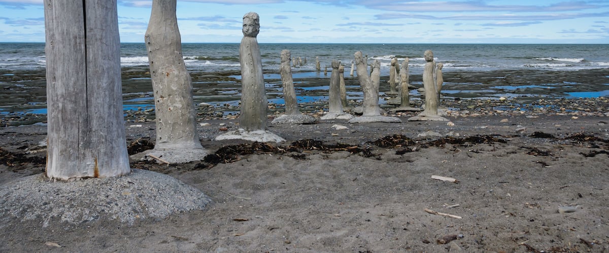 A row of stone statues on a beach with the ocean in the background.