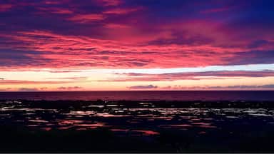 Un coucher de soleil sur un paysage côtier, avec des nuages rose vif et violets.
