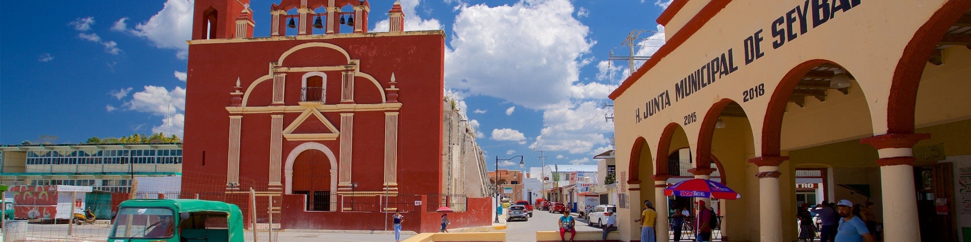 A historic church with a clock tower and a building with arches and a sign reading "H. Junta Municipal de Seybaplaya".