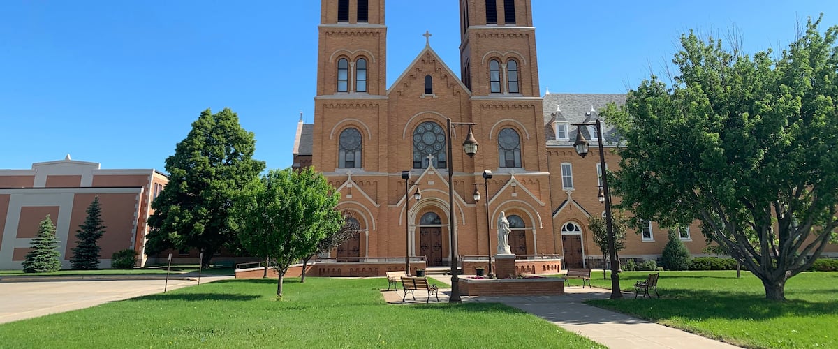 A large brick church with two towers and a statue in front.