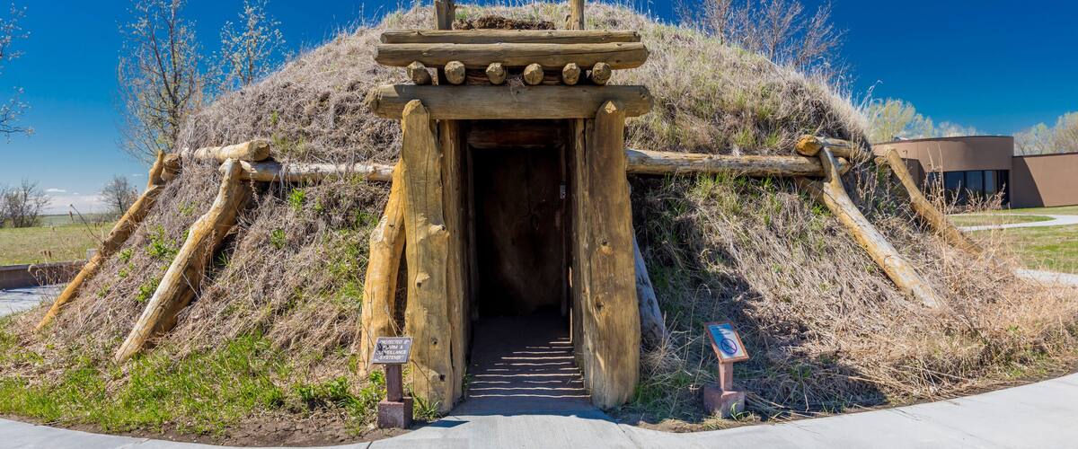 A large mound with a wooden entrance, surrounded by dry grass and trees.