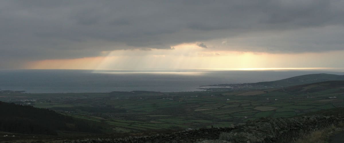 A coastal landscape with fields, a stone wall, and a stormy sky.