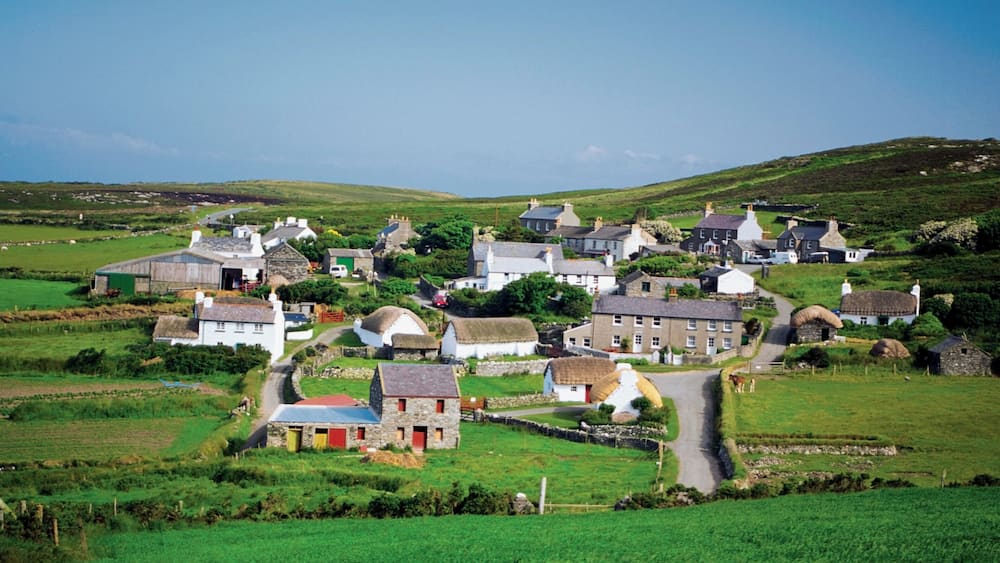 Un village rural avec des maisons en pierre, une route sinueuse et des champs verdoyants.
