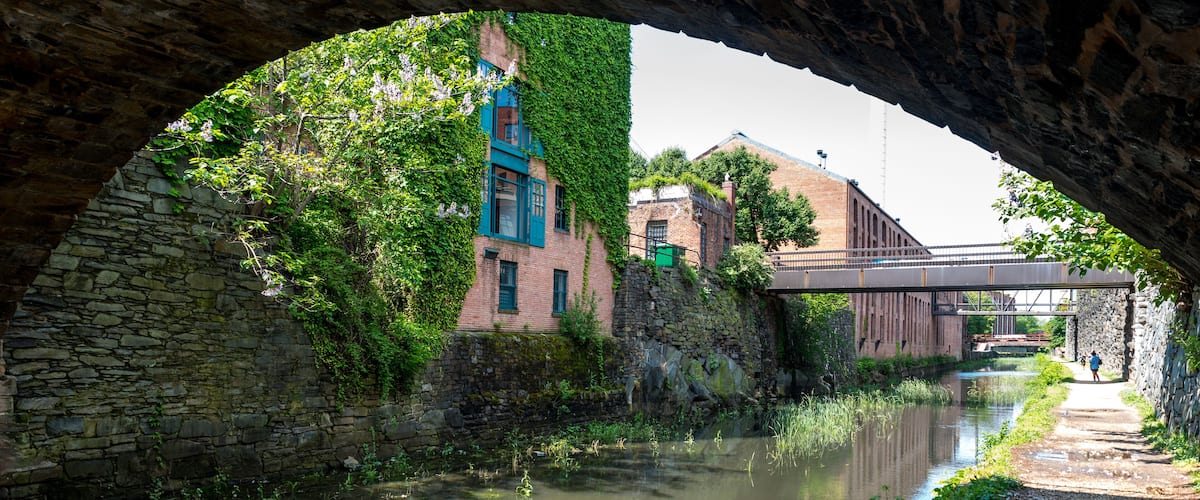 A stone bridge over a canal with buildings on either side, including one with blue shutters.