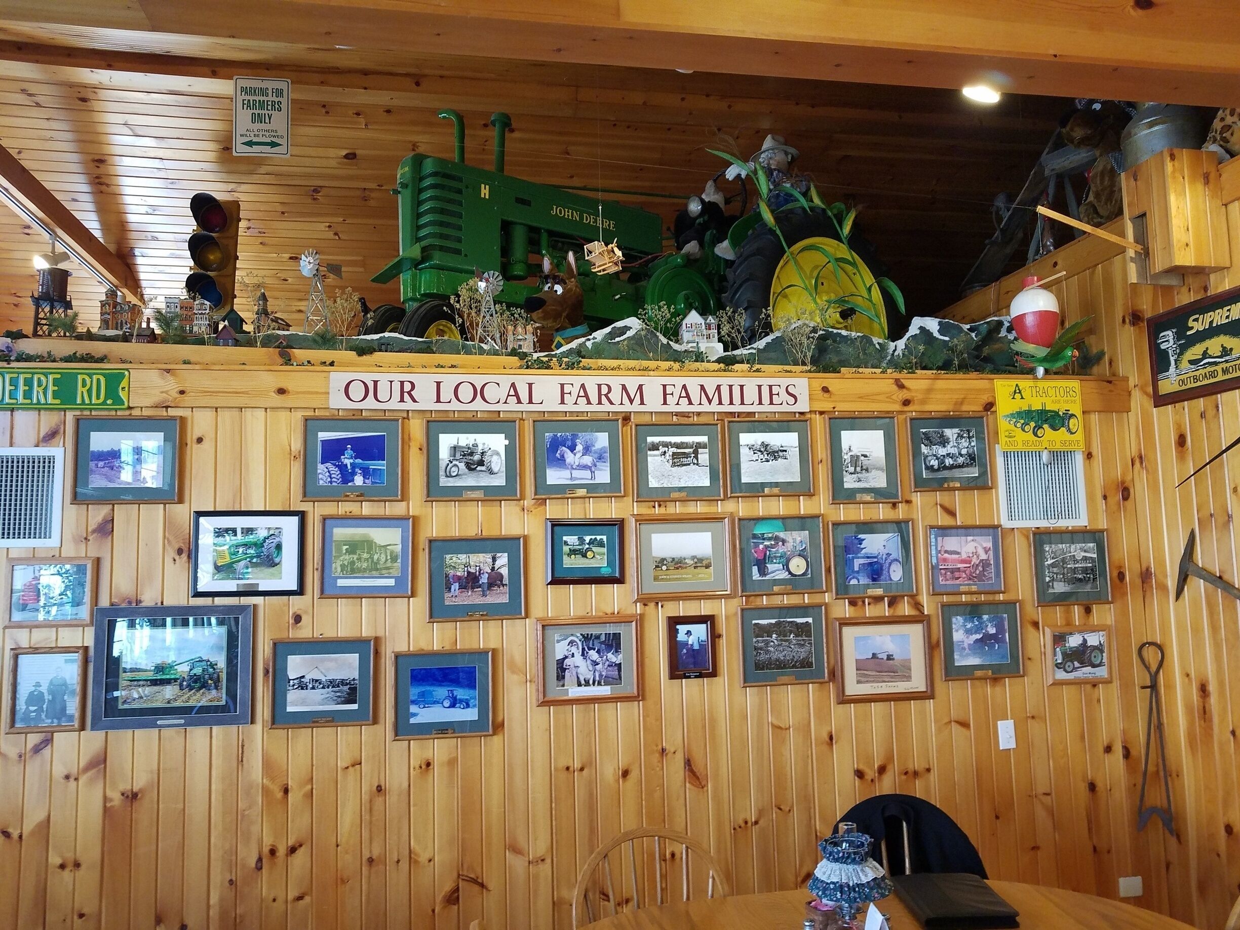 A wooden wall with framed photographs of local farm families and a green tractor.
