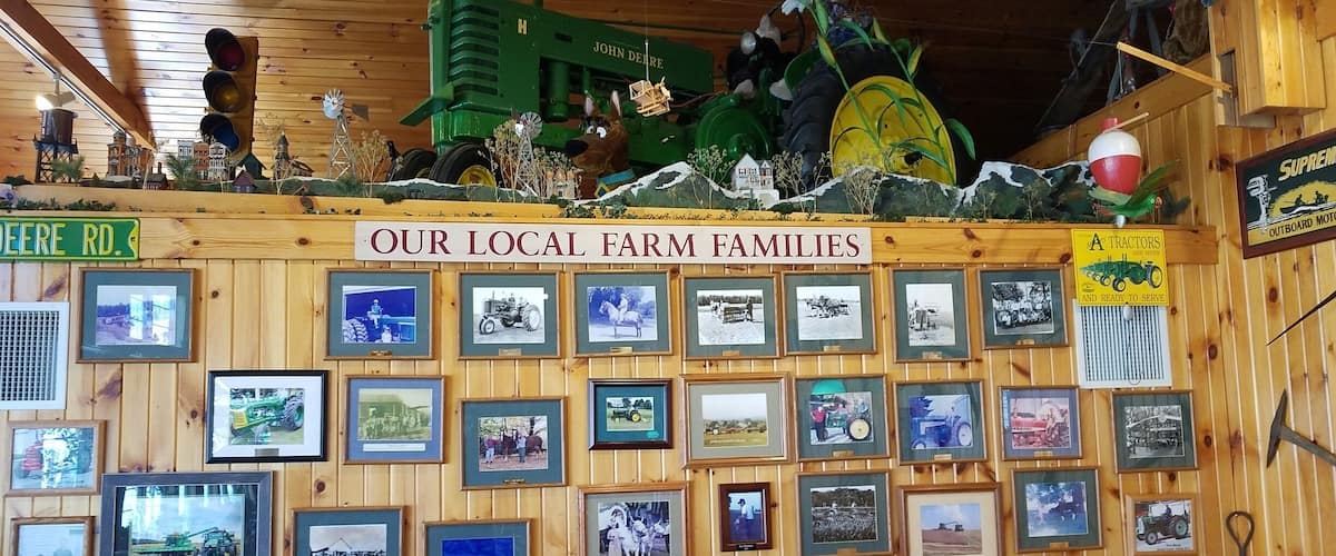 A wooden wall with framed photographs of local farm families and a green tractor.
