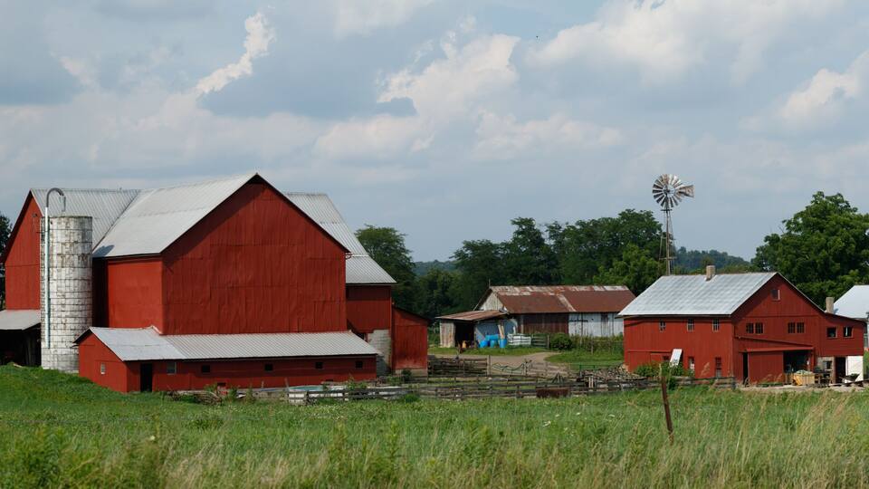 A red barn, a windmill, and a white house in a rural setting.