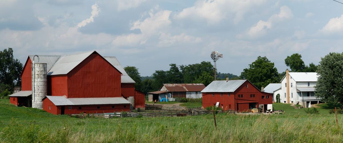 A red barn, a windmill, and a white house in a rural setting.