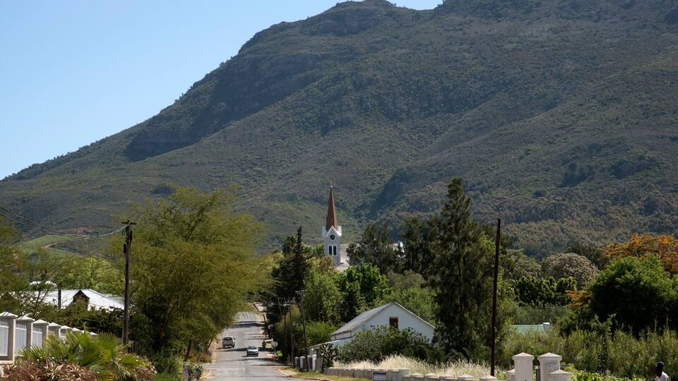 A rural road leading to a church with a steeple, surrounded by lush greenery and hills.