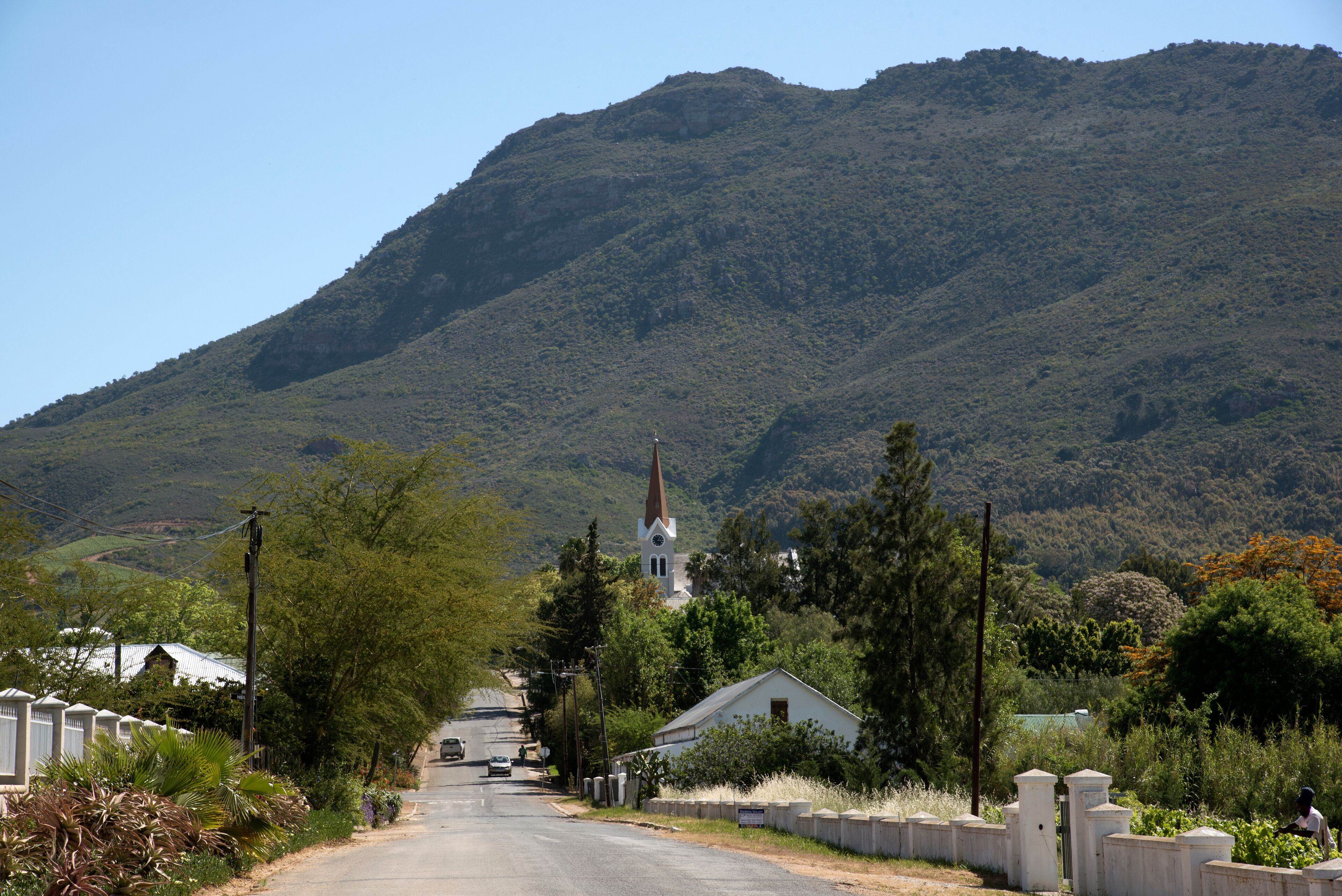 A rural road leading to a church with a steeple, surrounded by lush greenery and hills.