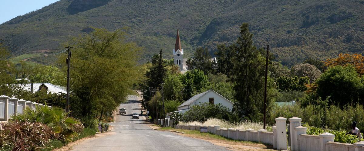 A rural road leading to a church with a steeple, surrounded by lush greenery and hills.