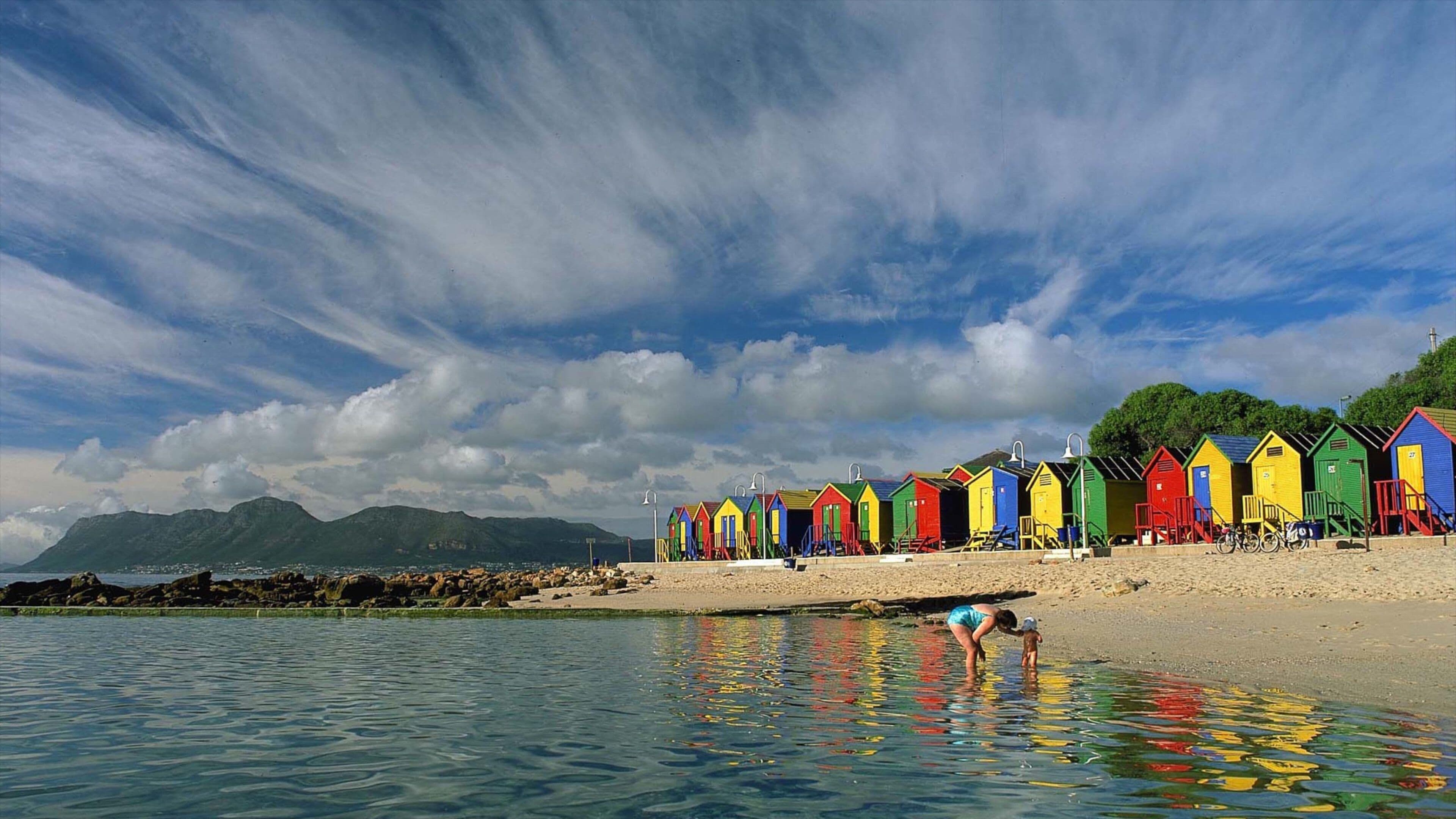 Uma praia com cabanas coloridas e um mar tranquilo.
