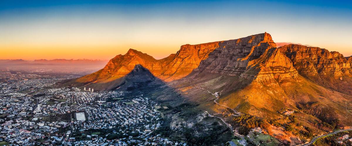 cape town aerial panorama from the table mountain at sunset, sun shining on the mountain range town in the dusk