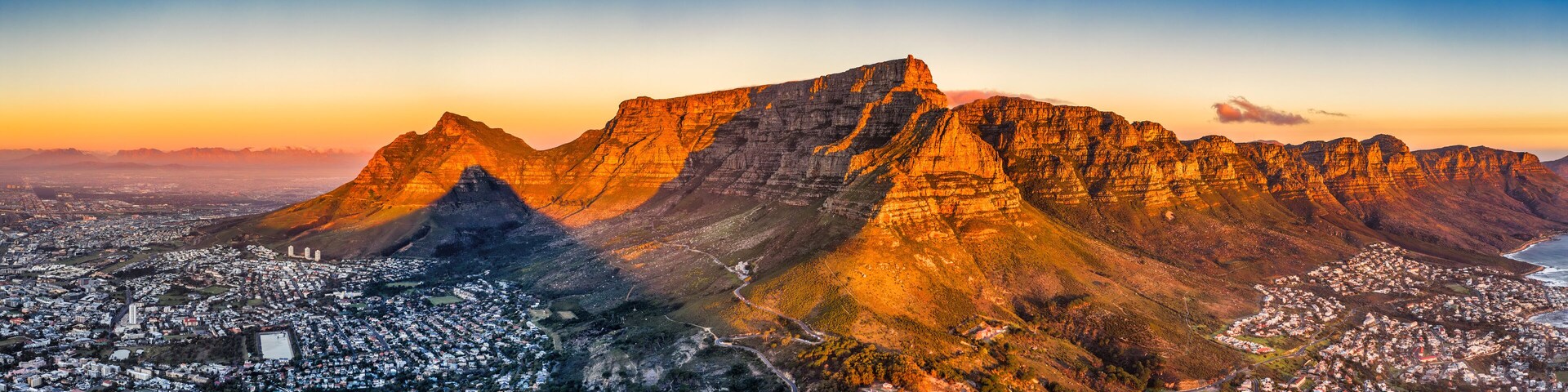 cape town aerial panorama from the table mountain at sunset, sun shining on the mountain range town in the dusk