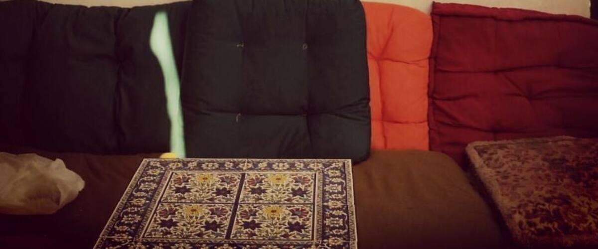 A living room with a black cat silhouette on the wall, a patterned rug, and a couch with orange and red cushions.