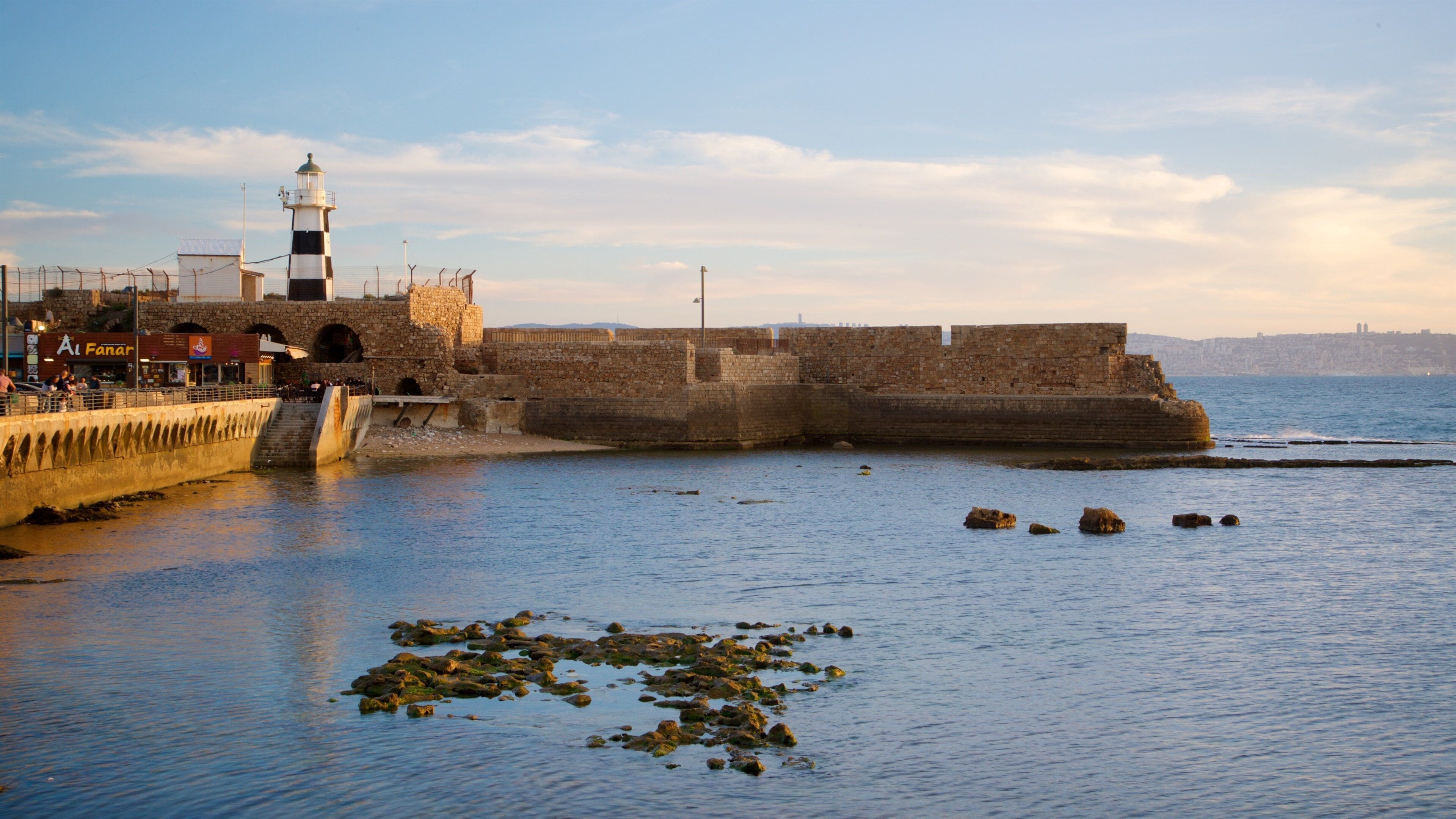 A coastal fortification with a lighthouse, rocky shoreline, and a clear sky.