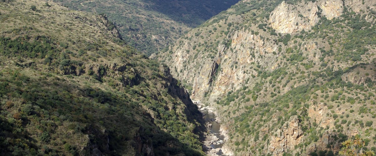 A canyon with a river running through it, surrounded by green hills and rocky cliffs.