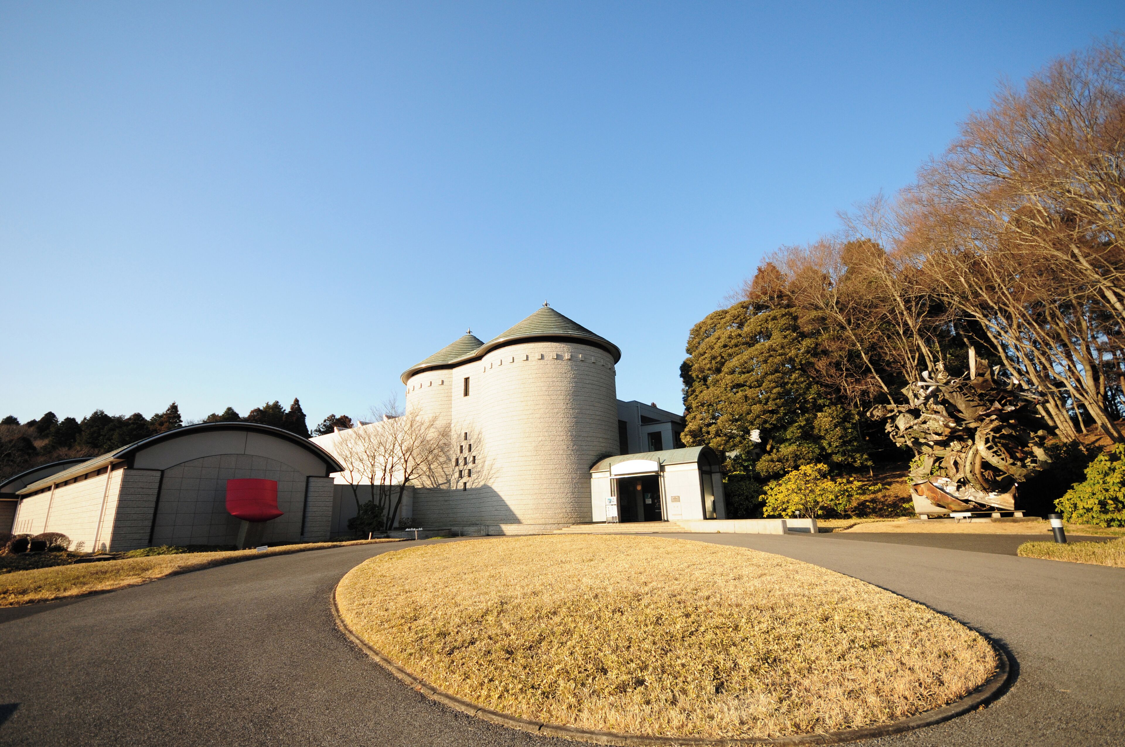 A historic tower with a round base and conical roof, surrounded by a paved area and trees.