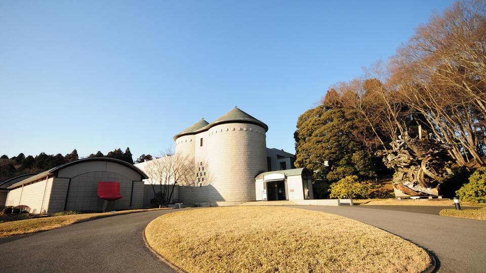 A historic tower with a round base and conical roof, surrounded by a paved area and trees.