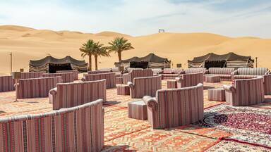 A desert landscape with sand dunes and a seating area with striped cushions and rugs.