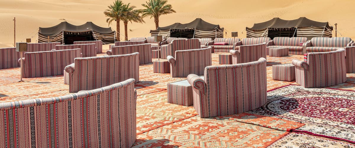 A desert landscape with sand dunes and a seating area with striped cushions and rugs.