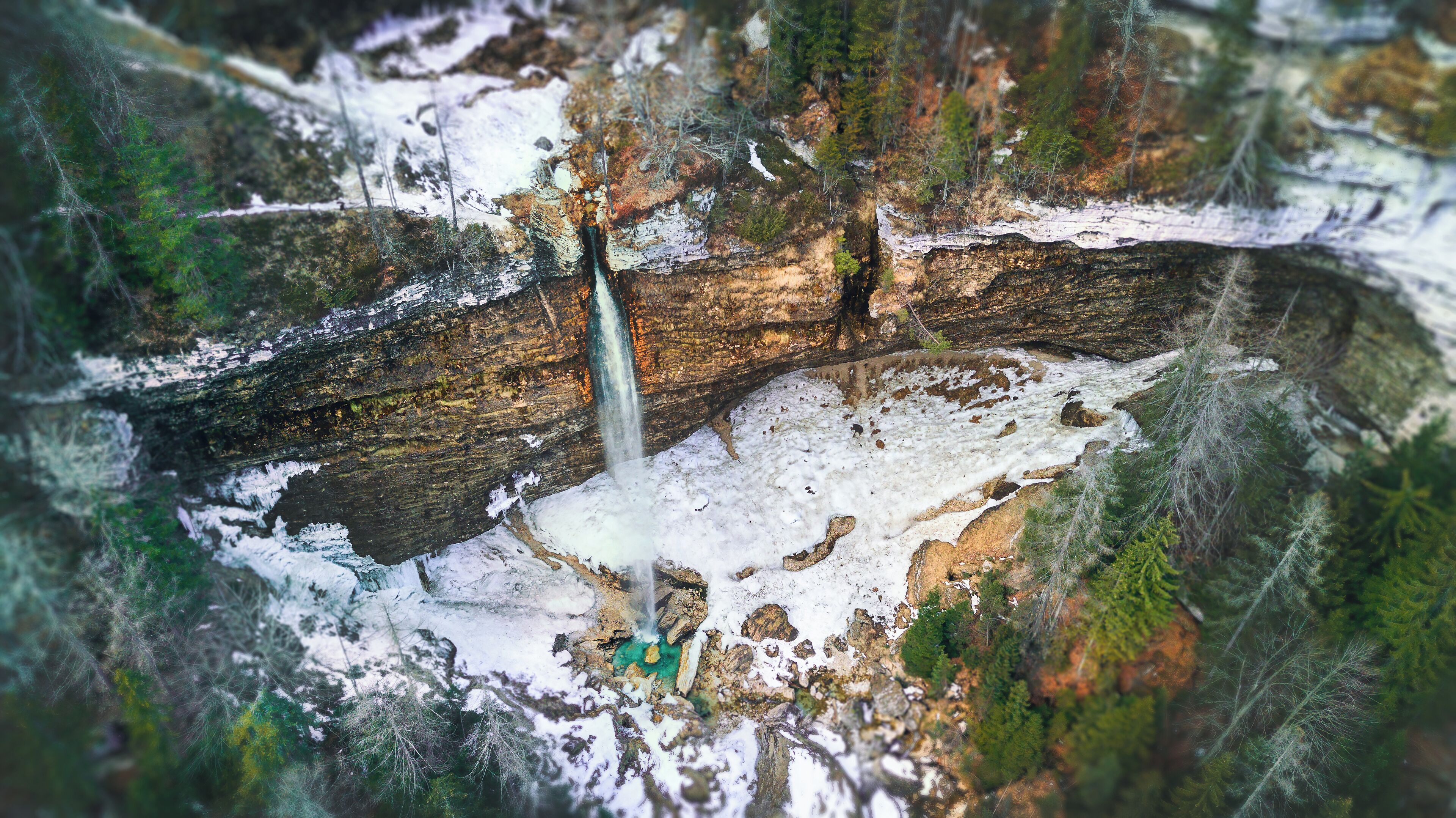 A waterfall cascading over a rocky cliff surrounded by snow and trees.
