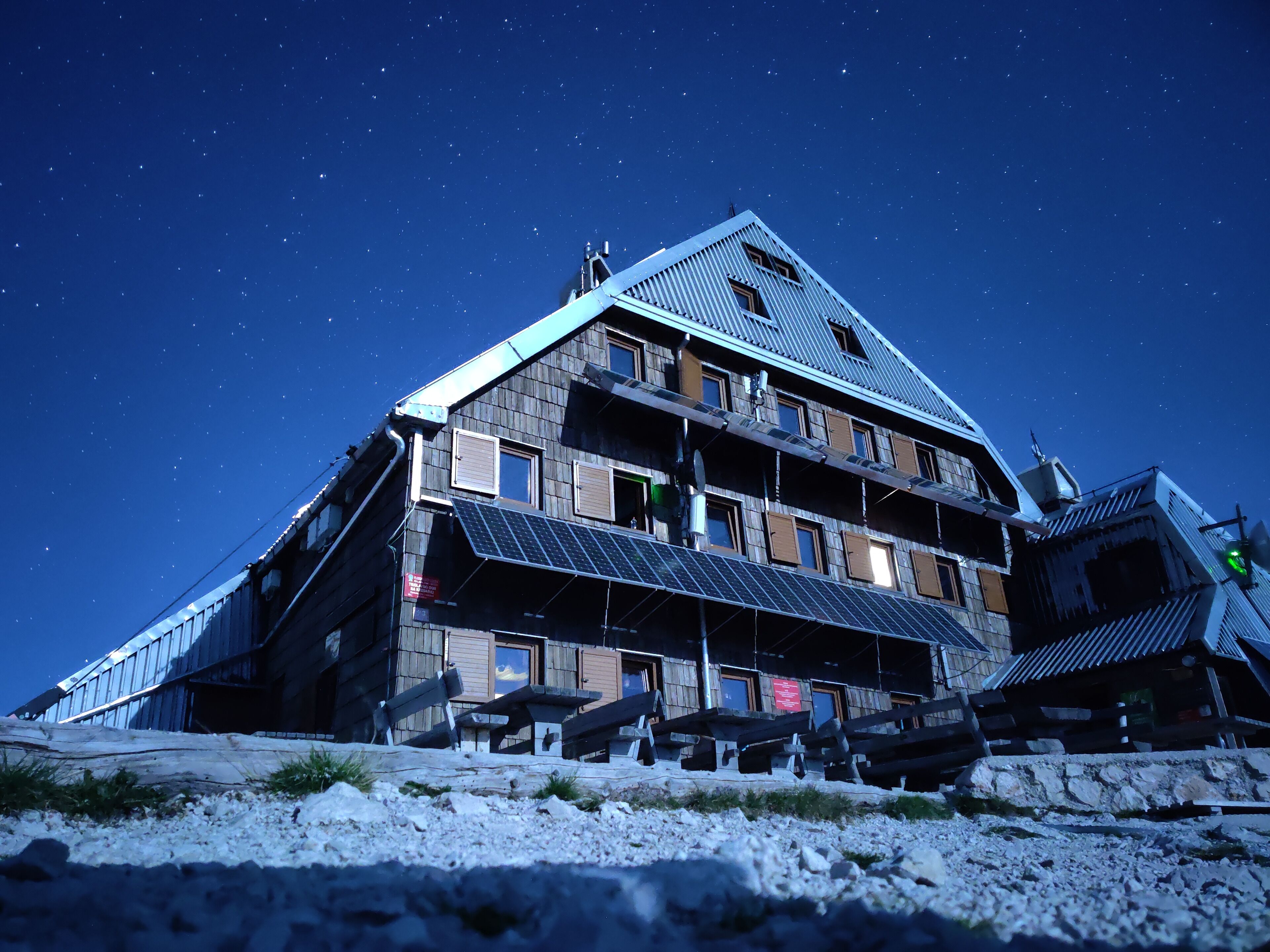 A multi-story building with a sloped roof, solar panels, and a starry night sky.