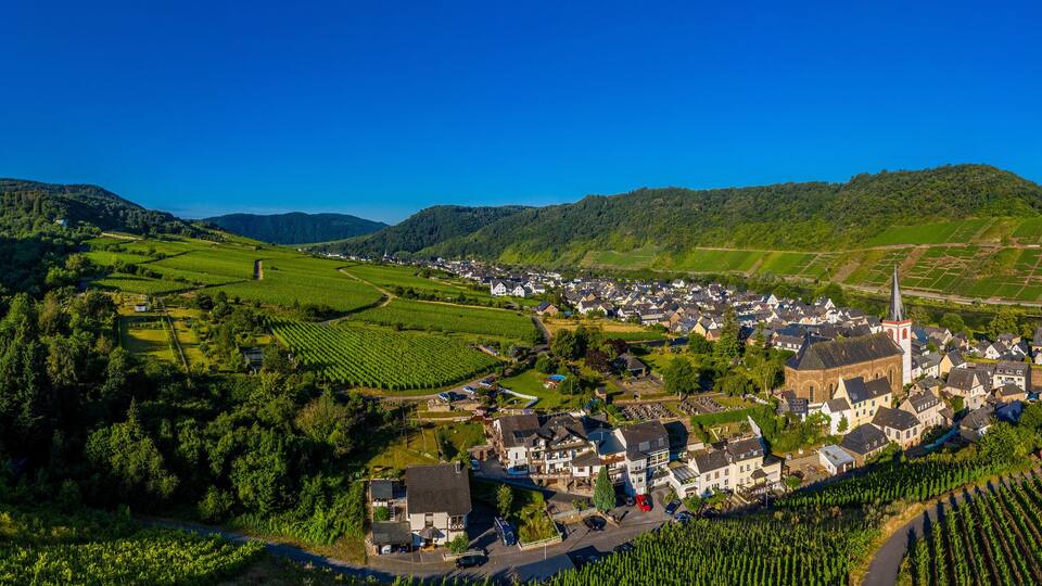 A village nestled in a valley surrounded by lush green hills and vineyards.