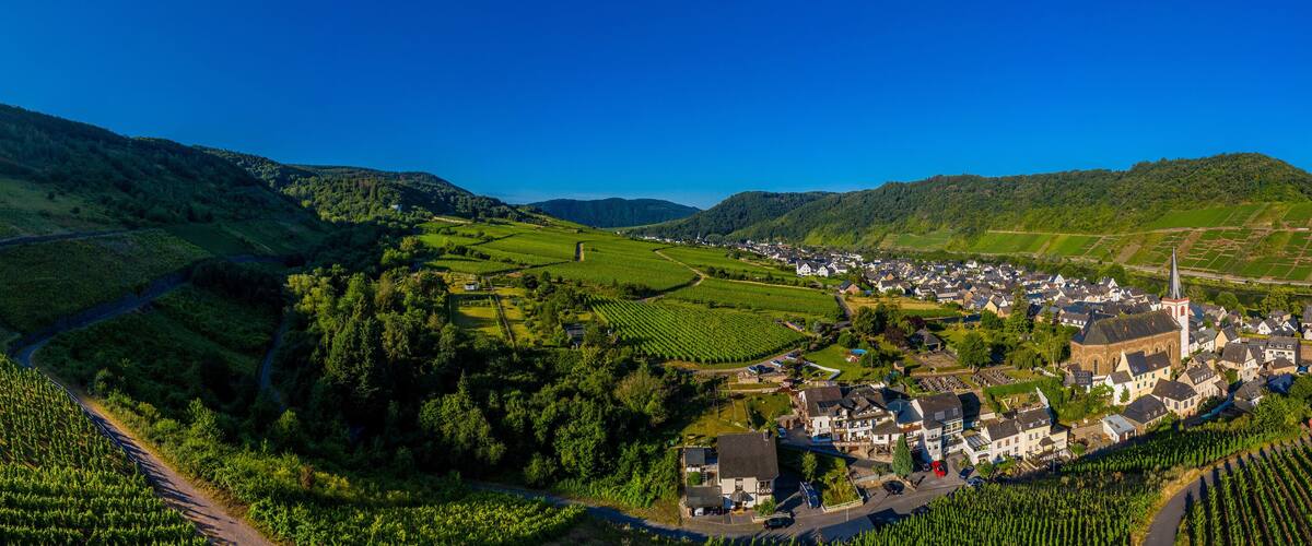 A village nestled in a valley surrounded by lush green hills and vineyards.