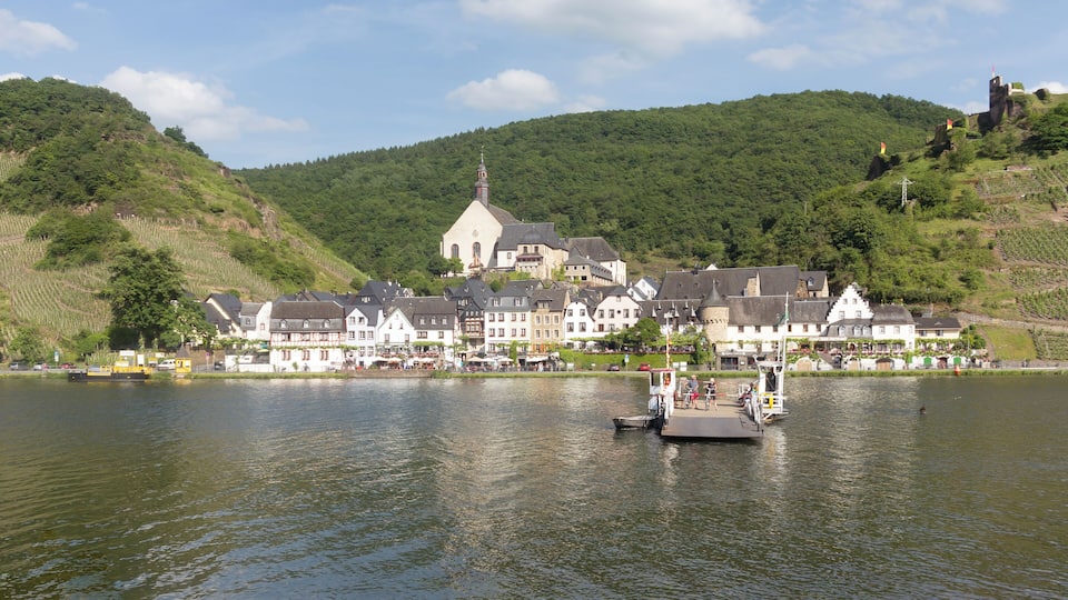A riverside town with historic buildings, a church, and a boat docked in the water.
