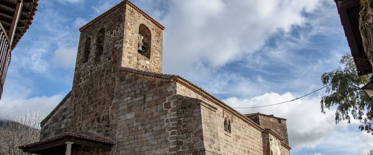 A historic stone church with a bell tower, parked cars, and a cobblestone street.