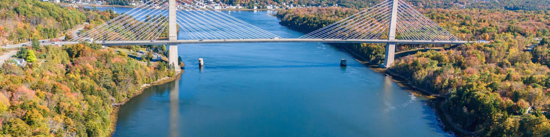 A suspension bridge over a river with surrounding autumn foliage and distant hills.