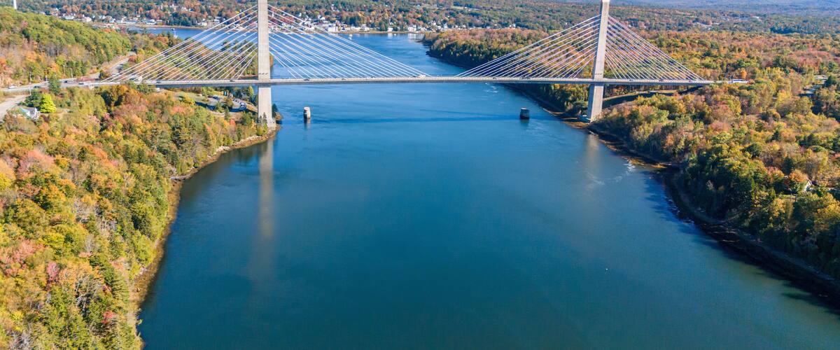 A suspension bridge over a river with surrounding autumn foliage and distant hills.