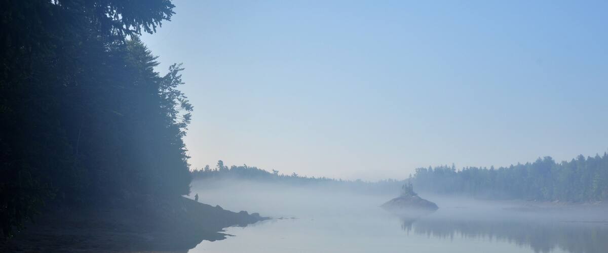 A calm lake with a forested shoreline and a misty atmosphere.