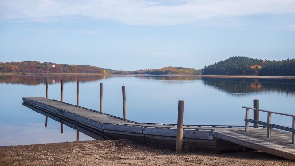 A calm lake with a wooden dock extending into the water, surrounded by hills with autumn foliage.