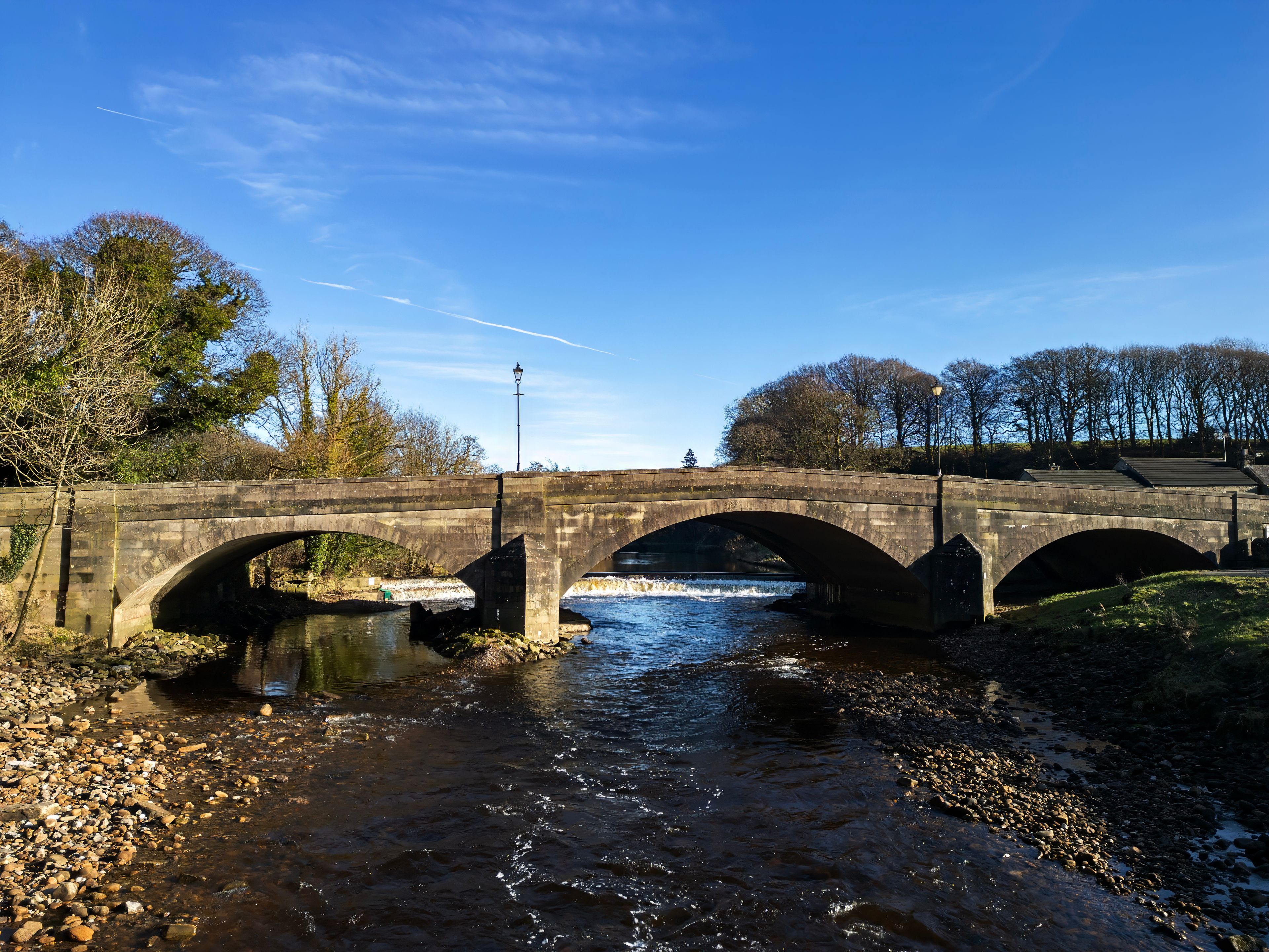Eine Steinbrücke über einem Fluss mit blauem Himmel und Bäumen im Hintergrund.