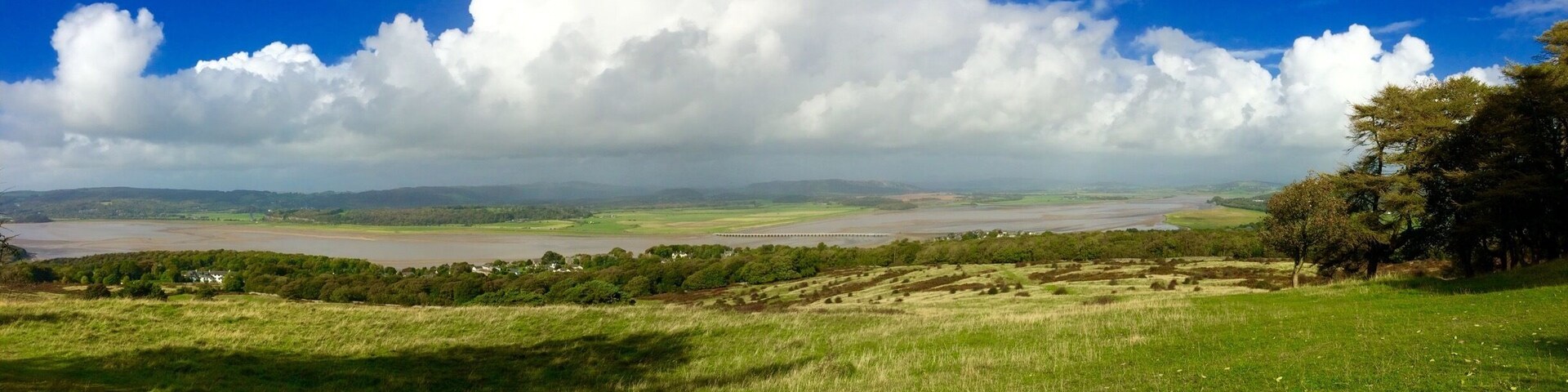 A river valley with a bridge, rolling hills, and scattered trees.